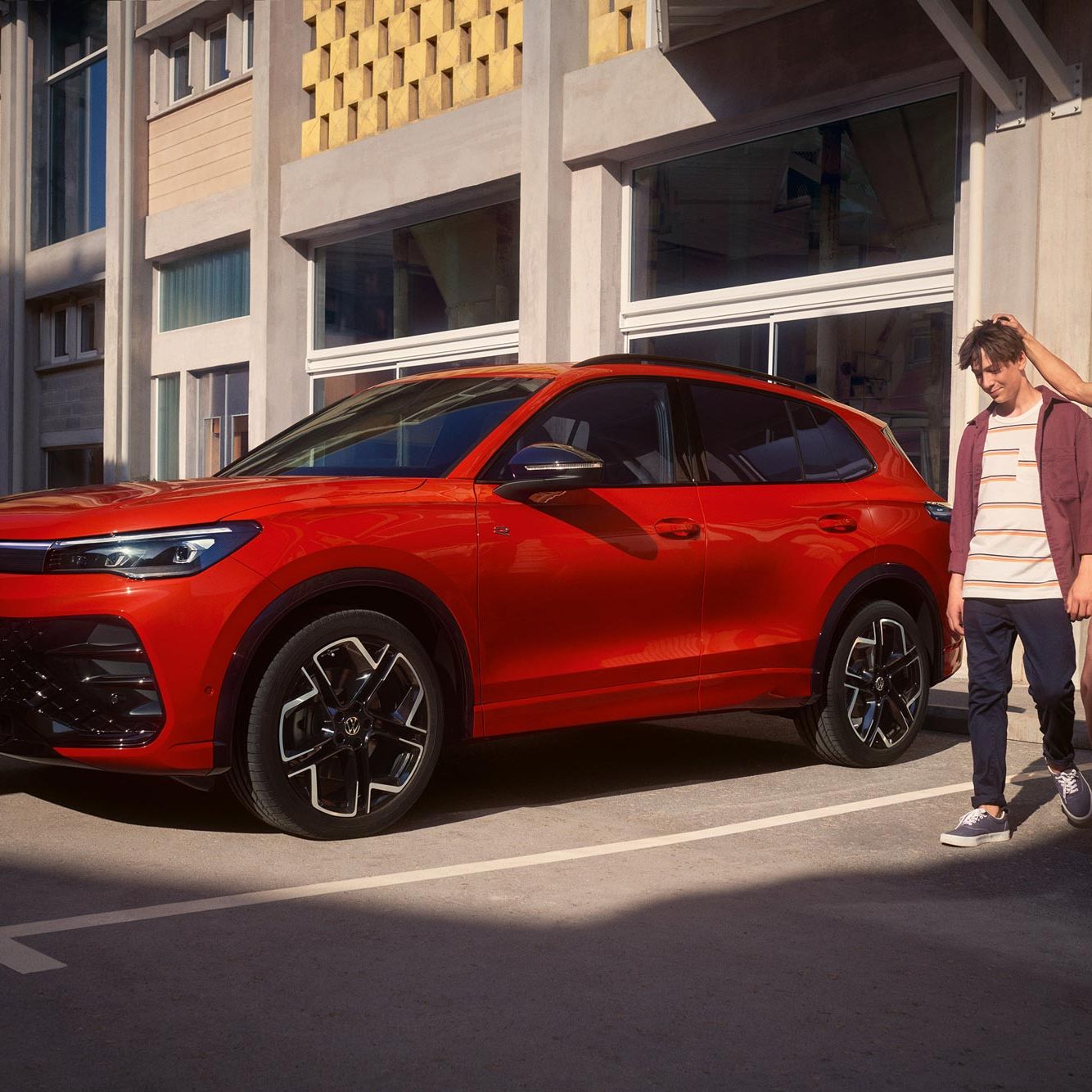 Mutter legt ihre Hand den Kopf ihres Sohnes, beiden gehen neben eines roten VW Tiguan R-Line her