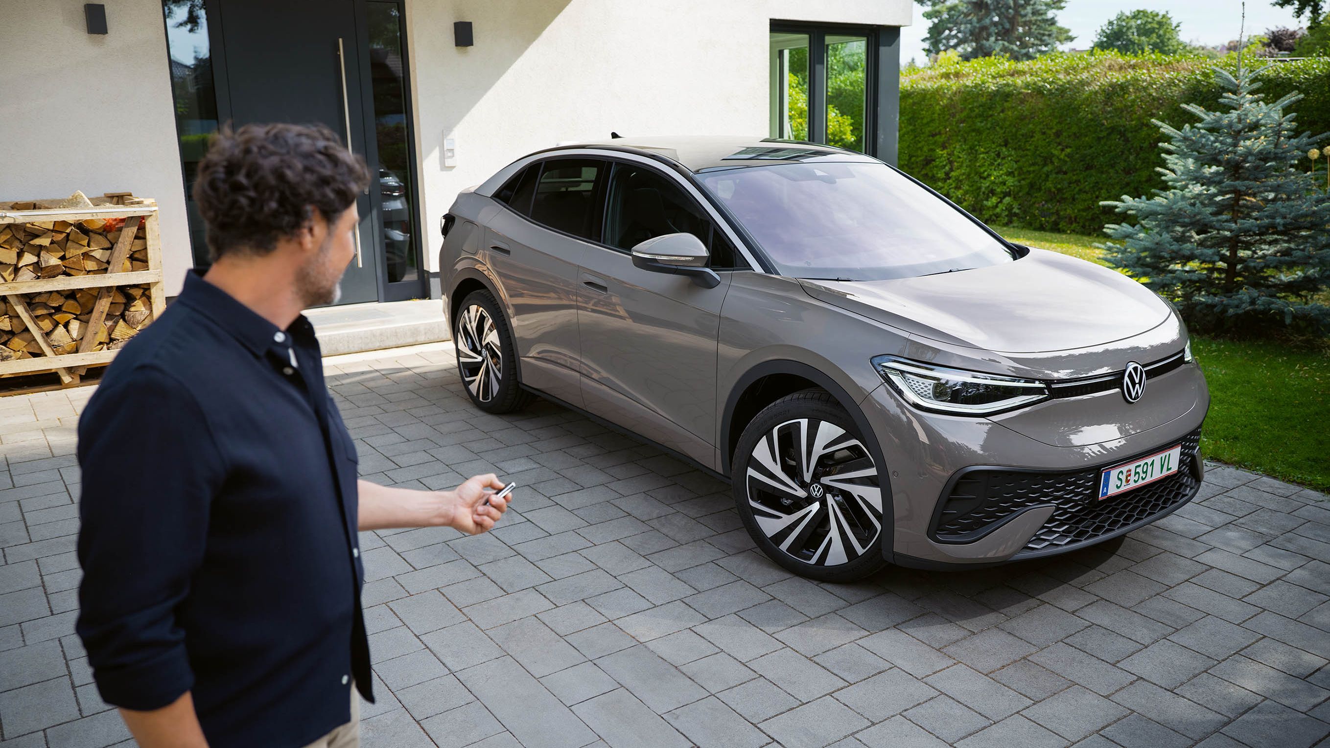 Ein grauer ID.5 steht in einer Einfahrt vor einem Haus, ein Mann schließt das Auto ab. 