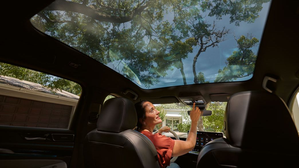 Frau sitzt in VW ID.7 und bedient per Knopfdruck das Sonnenrollo des Panoramadachs
