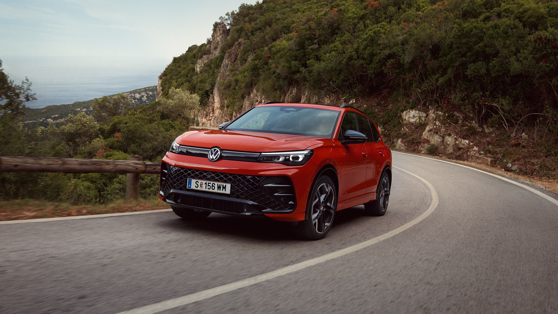 Roter VW Tiguan R-Line fährt eine kurvige Straße entlang.