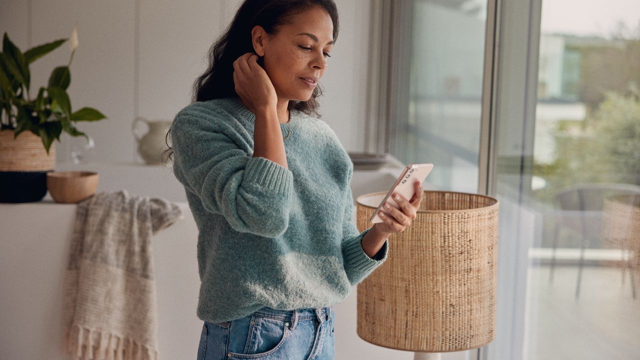 Eine Frau steht am Fenster und blickt auf ihr Smartphone