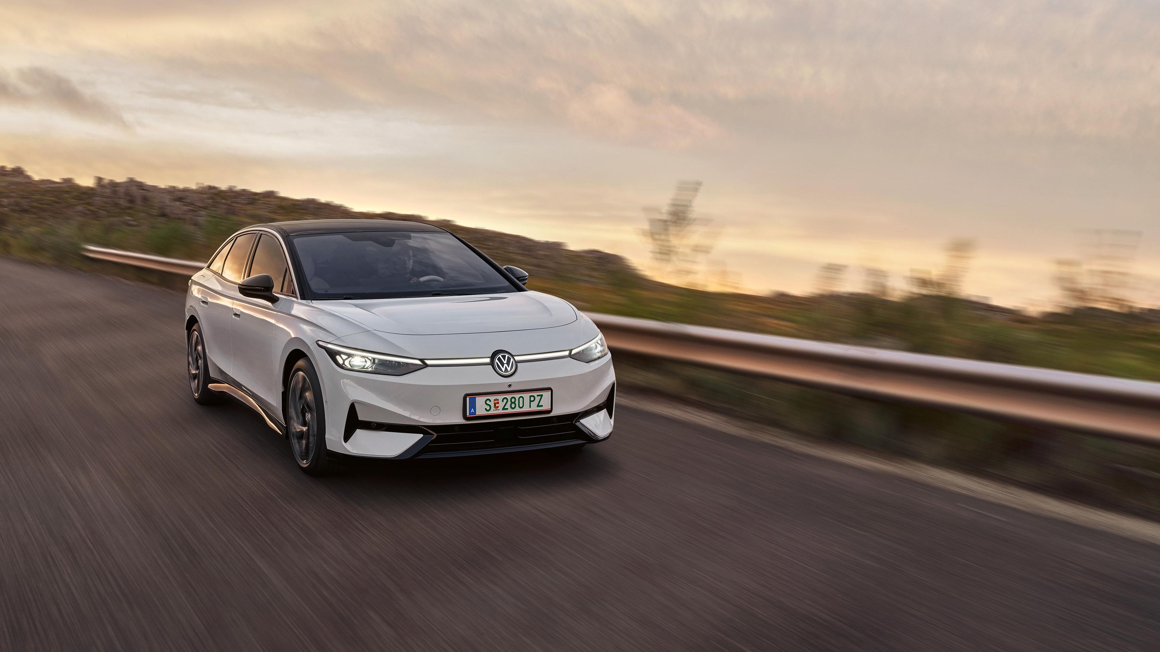 Frontansicht eines weißen VW ID.7, der über eine Landstraße fährt. 