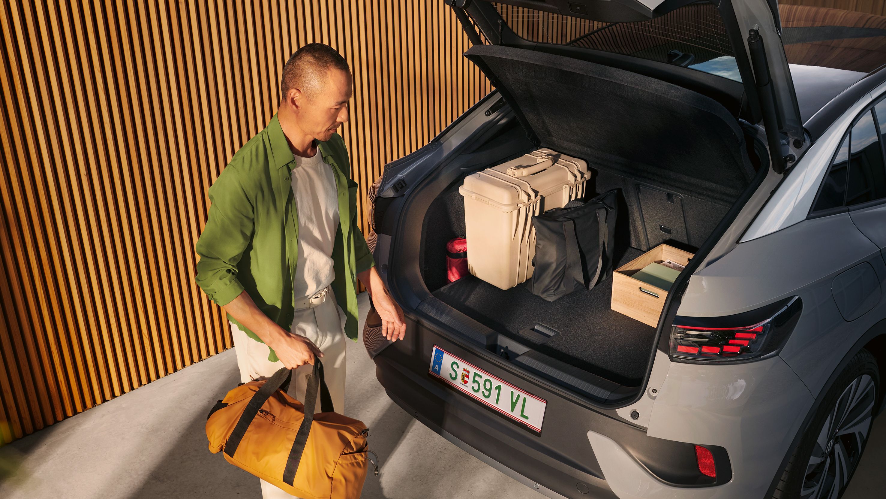 VW ID.5 mit geöffnetem Kofferraum und Gepäck darin, unter der offenen Heckklappe steht ein Mann mit einer Tasche in der Hand