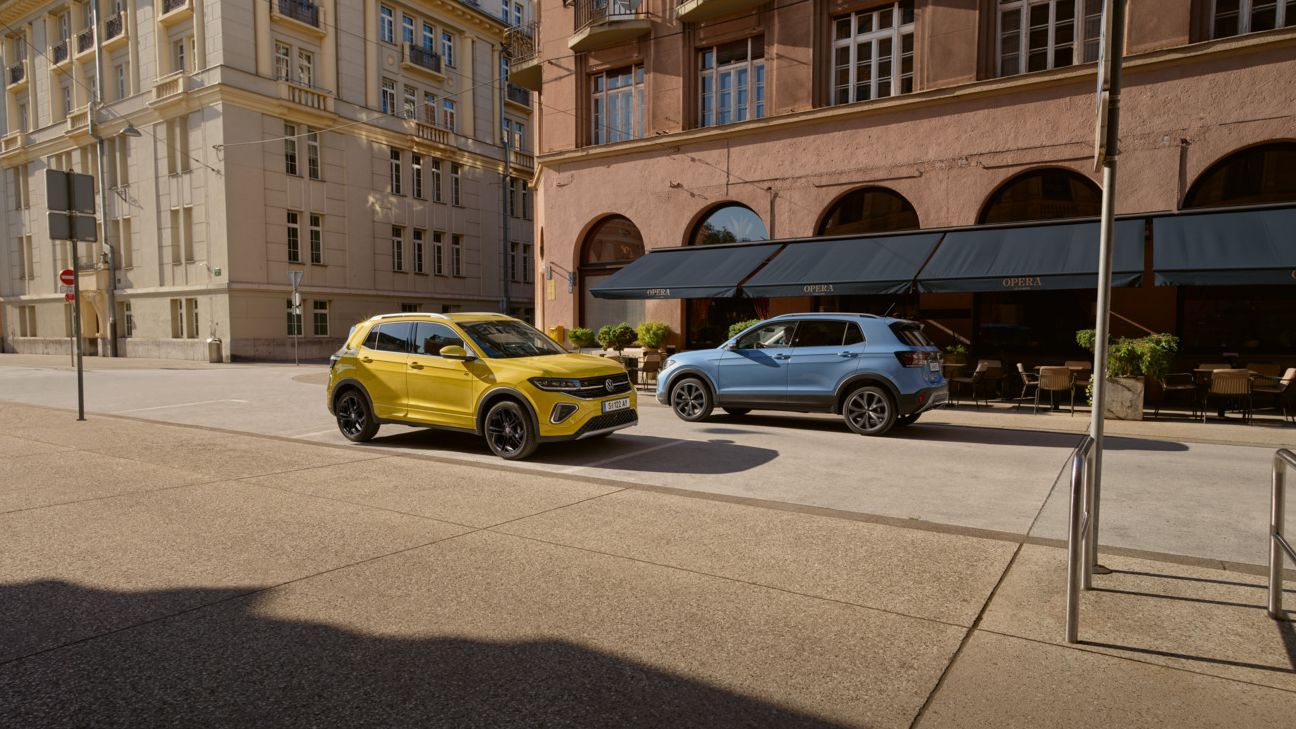 Ein gelber und ein blauer VW T-Cross fahren auf einer Straße aneinander vorbei.