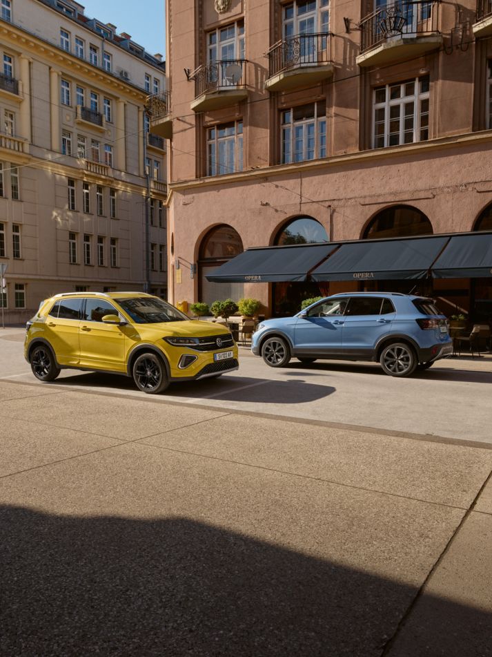 Ein gelber und ein blauer VW T-Cross fahren auf einer Straße aneinander vorbei.