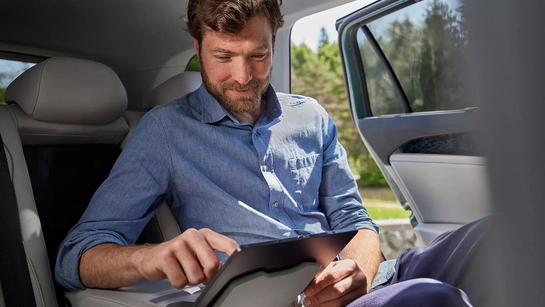 Mann sitzt auf Rückbank im VW Passat und bedient Tablet das in der Halterung befestigt ist