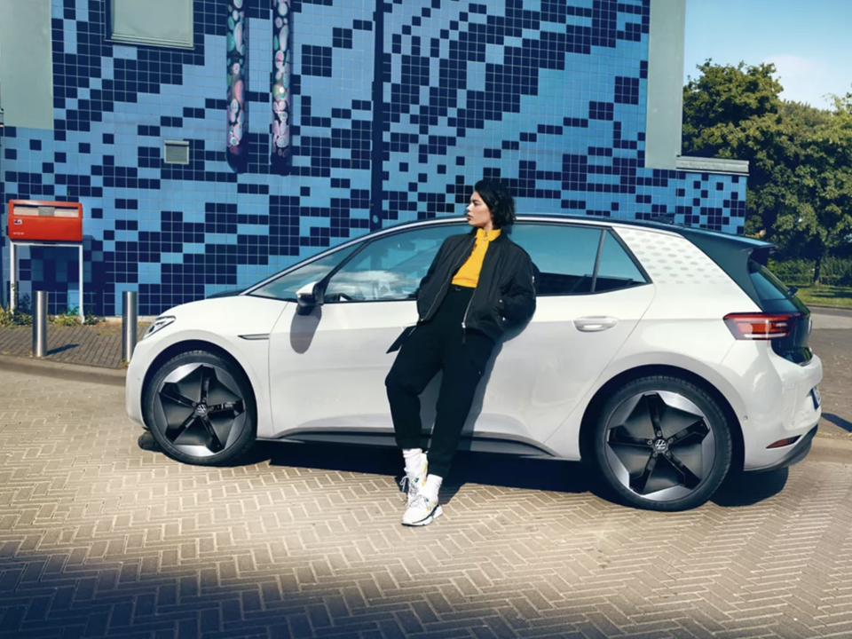 Gruaja mbështet në VW ID.3 të parkuar buzë rruge