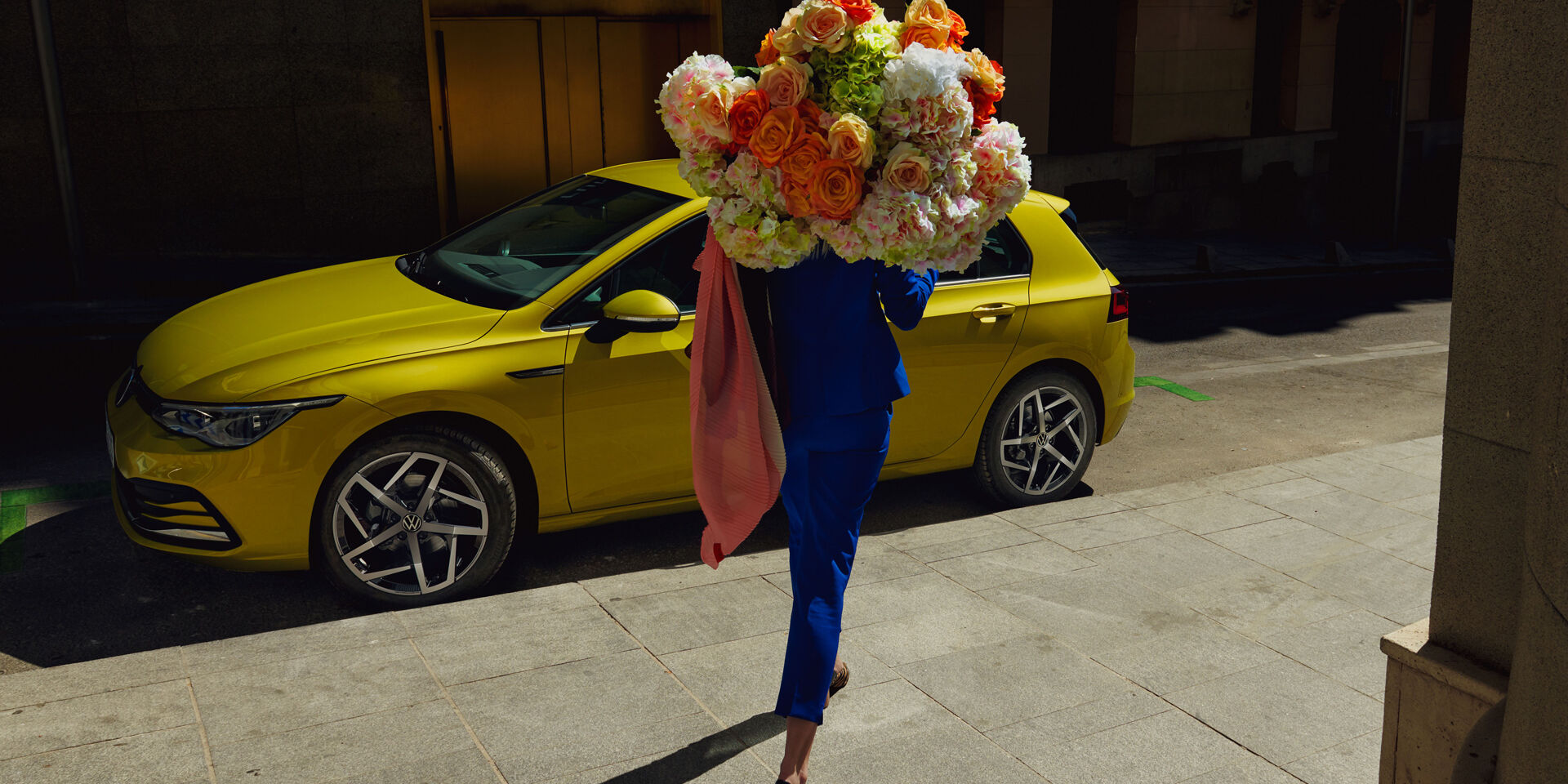 VW Golf Seitenansicht, Frau geht mit Blumenstrauß auf ihn zu