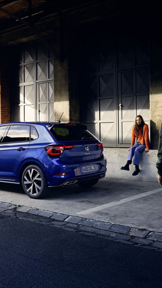 Ein blauer VW Polo steht vor einer Rampe, ein Mann geht am Heck mit den optionalen LED-Rückleuchten vorbei. 