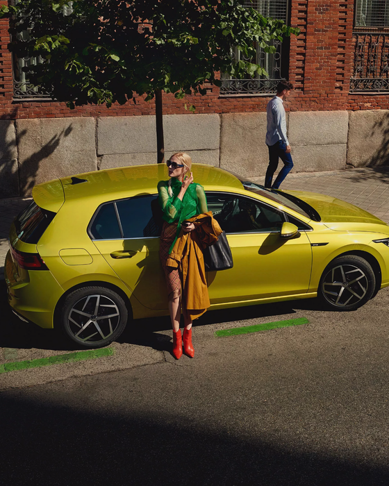 VW Golf parkt am Straßenrand, eine Frau lehnt an der Seitentür