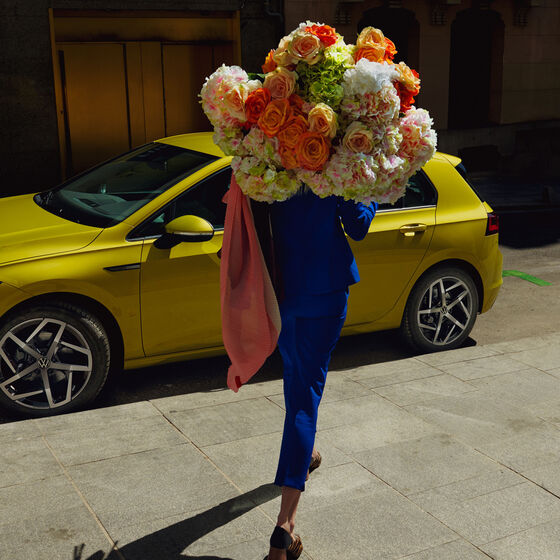 VW Golf Seitenansicht, Frau geht mit Blumenstrauß auf ihn zu